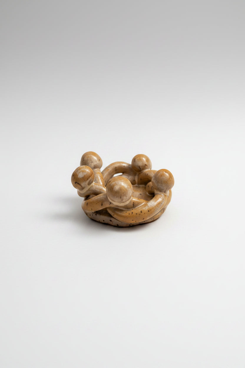 Small ceramic sculpture of a group of people huddled together on a plain background